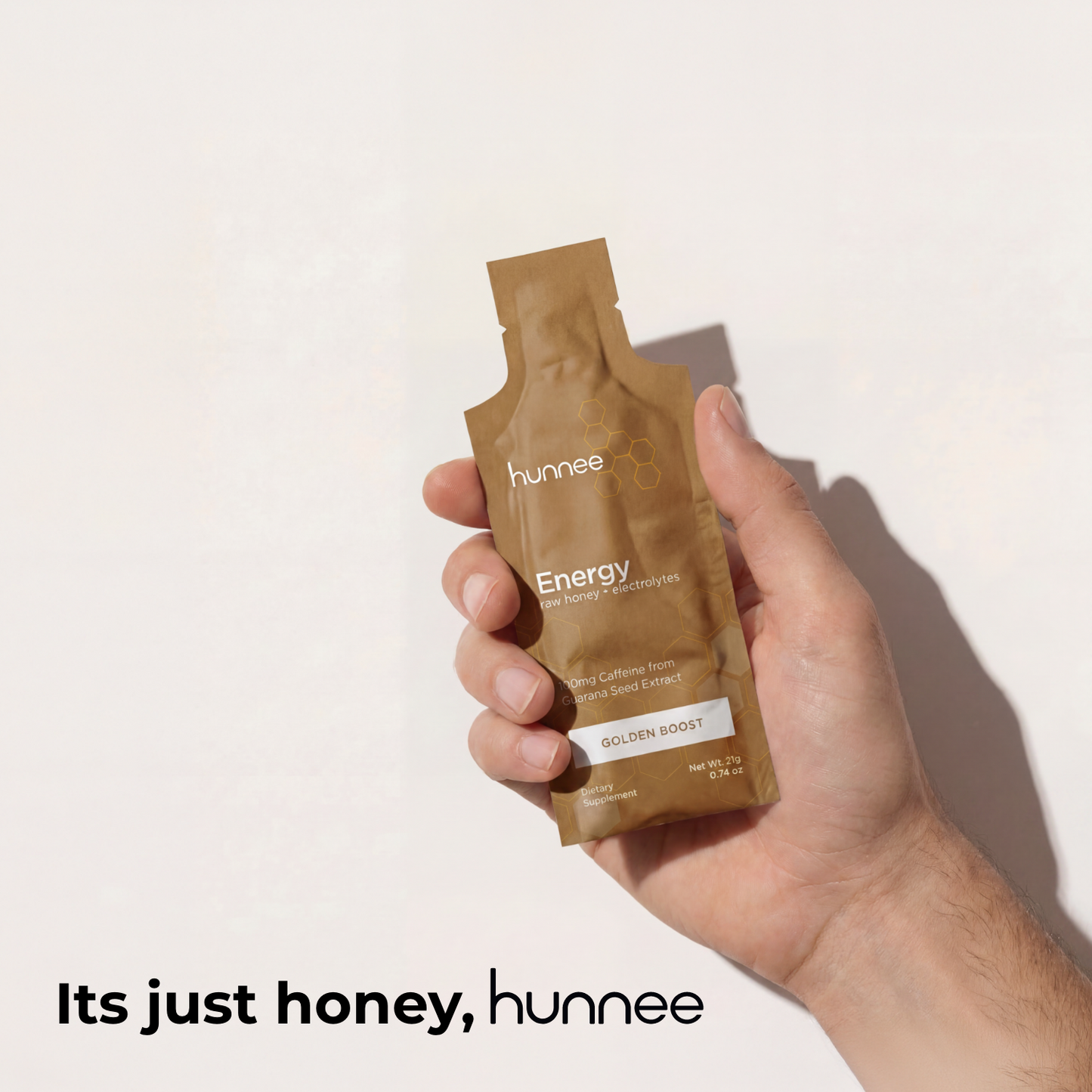 Hand holding a brown 'hunnee' energy drink mix packet against a light background