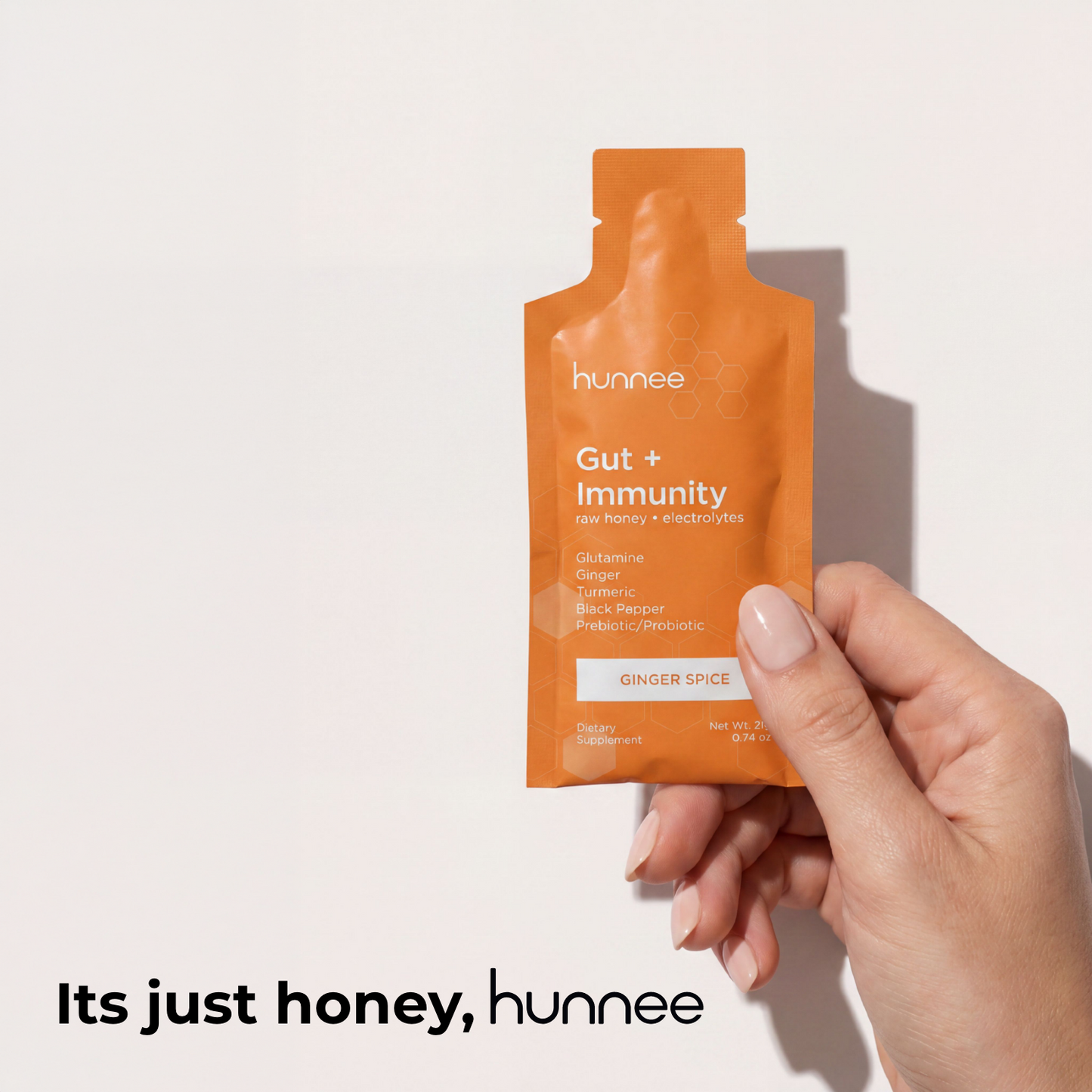 Hand holding an orange 'hunnee' packet labeled 'Gut + Immunity' on a light background