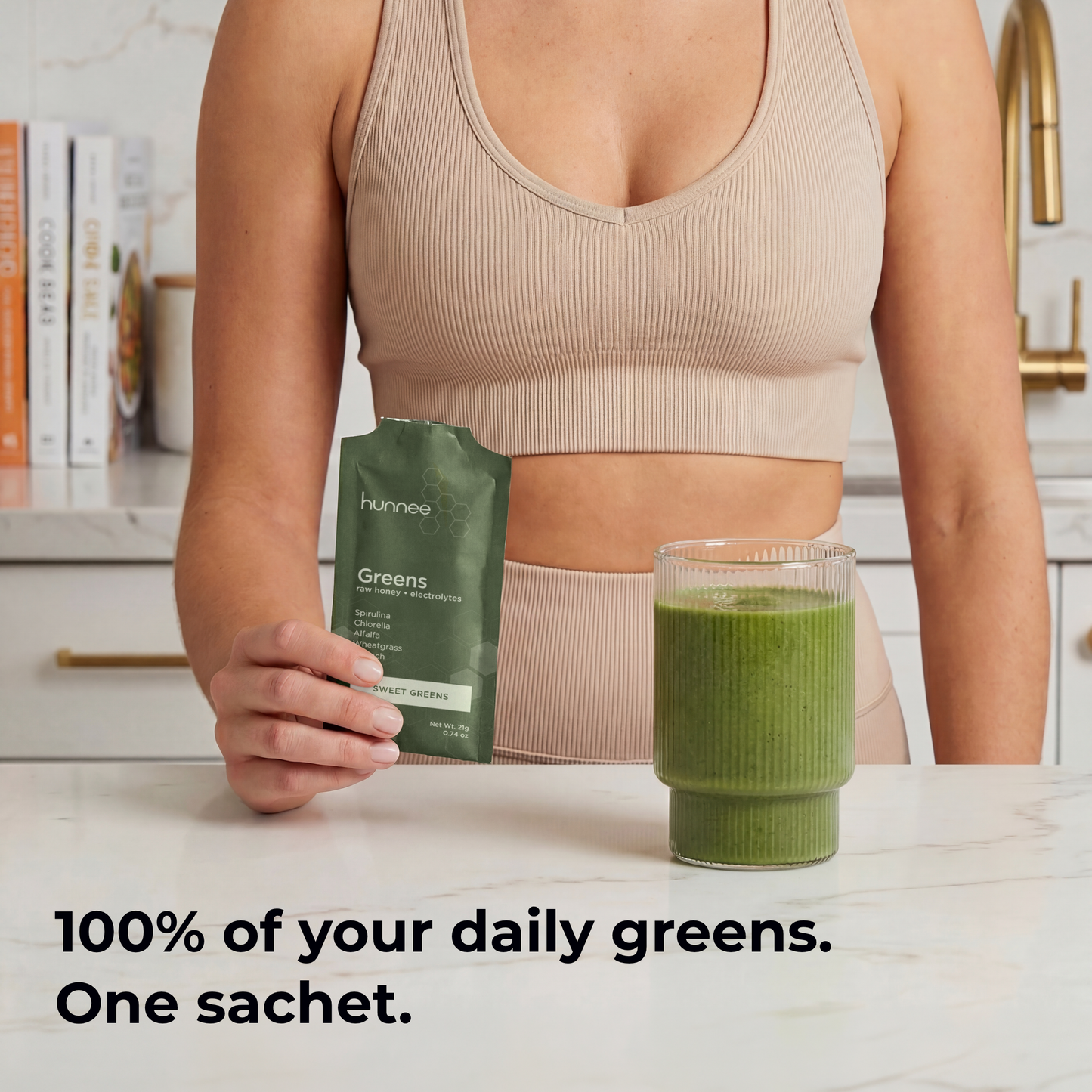 Person holding a green smoothie package with a glass of green smoothie on a kitchen counter.