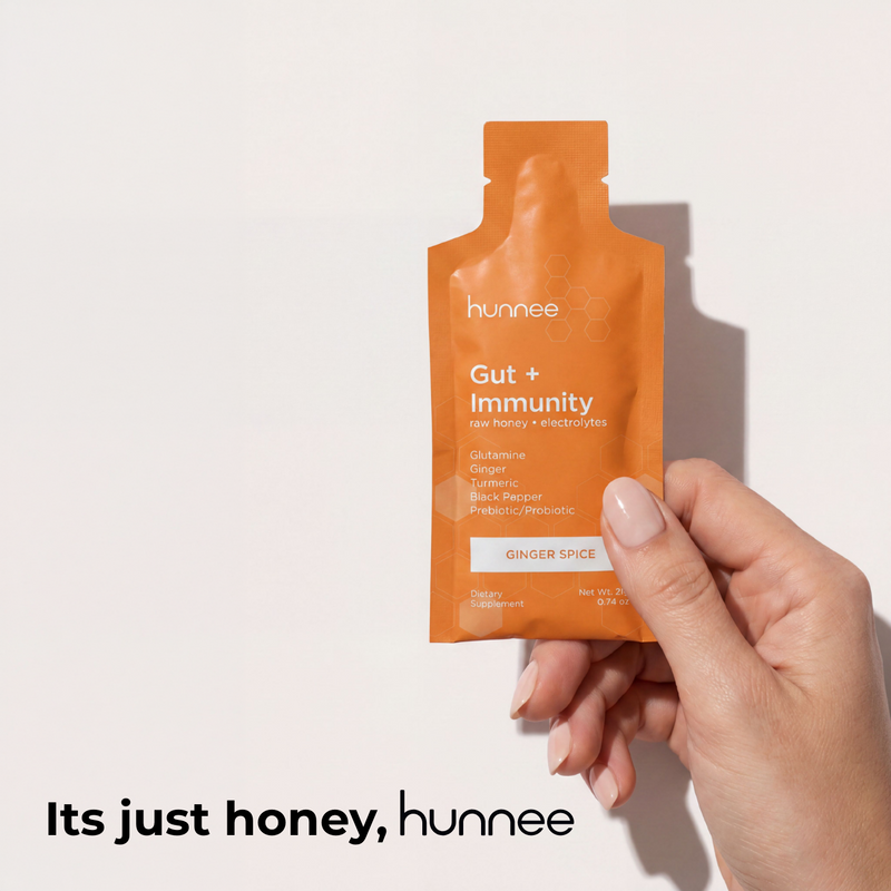 Hand holding an orange 'hunnee' packet labeled 'Gut + Immunity' on a light background