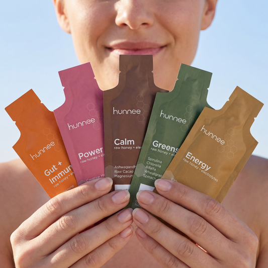 Person holding five hunnee product packets against a clear blue sky.